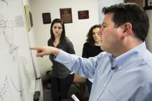 Researcher Brian Denton stands at whiteboard instructing his graduate students