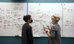 Amy Cohn talks to a student in front of a whiteboard full of equations