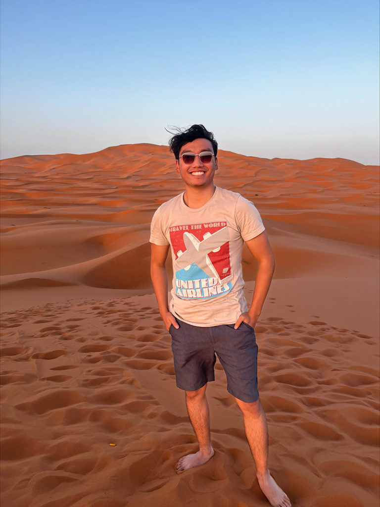 Nick Tran stands on a sand dune wearing a United Airlines shirt.
