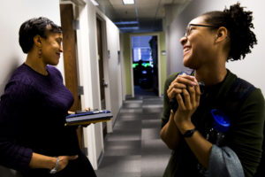 A professor talks with a smiling student in a hallway