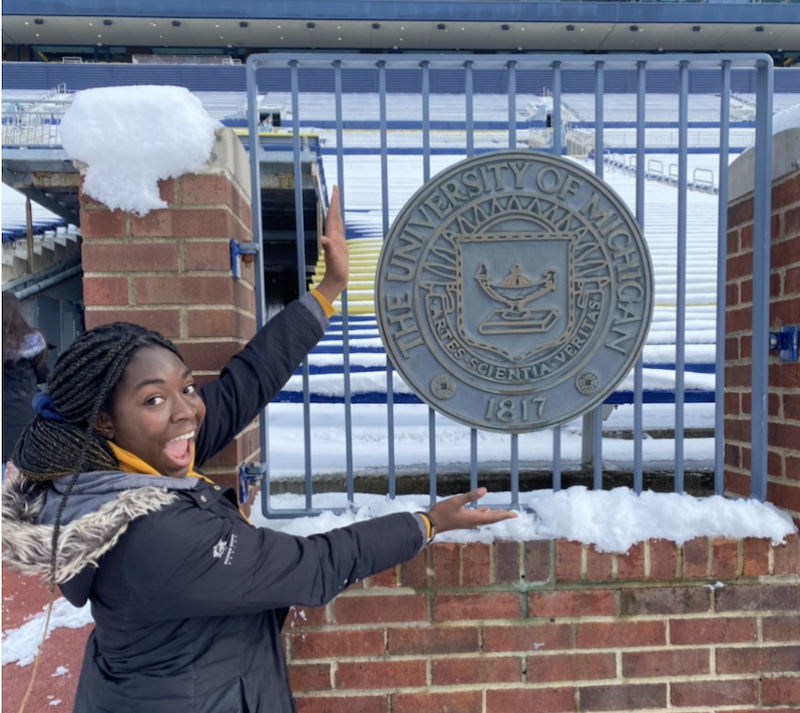 Person smiles in front of University of Michigan sign