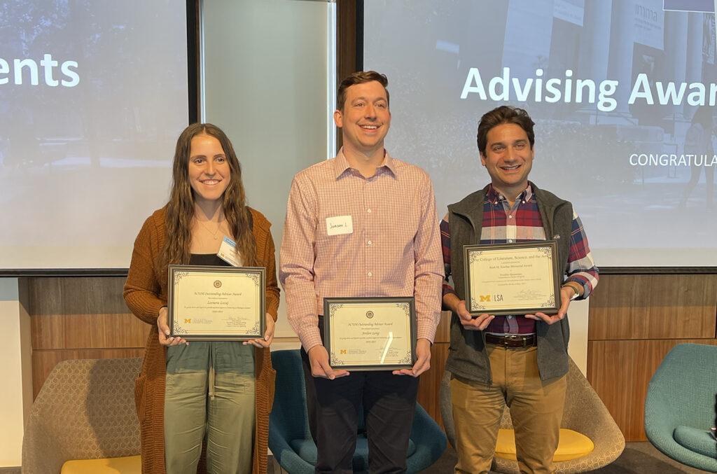Three people smile with there advising awards from the University of Michigan