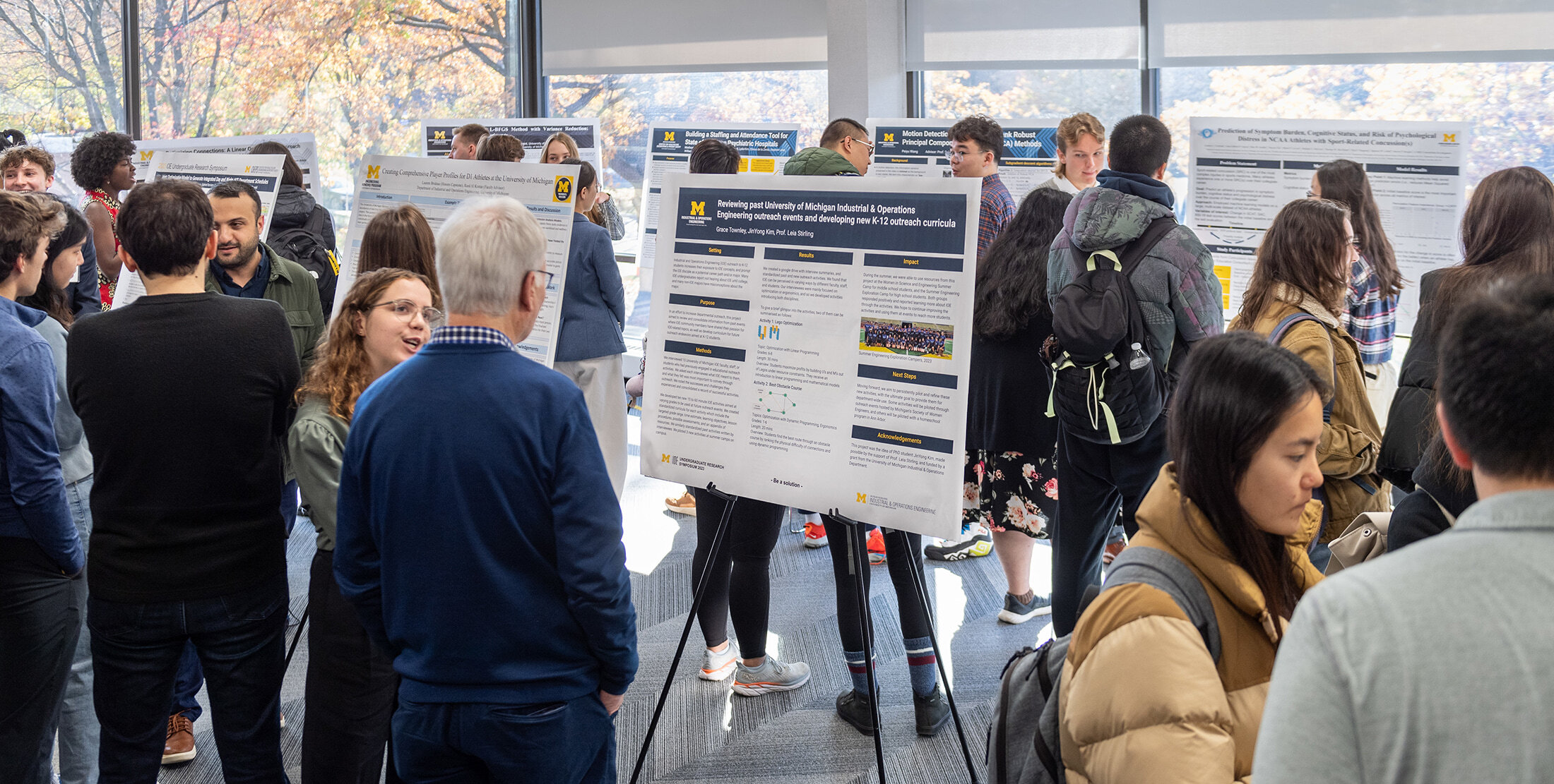 Many people in warm clothing rotate around a crowded room while looking at research posters