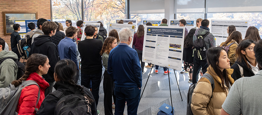 A crowded room of people look at various research posters