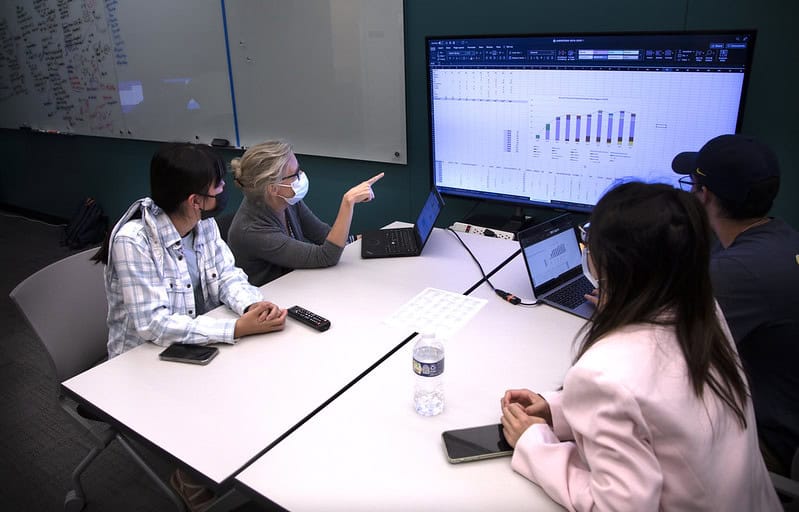 Four people sit around a table looking at a screen with graphs on in