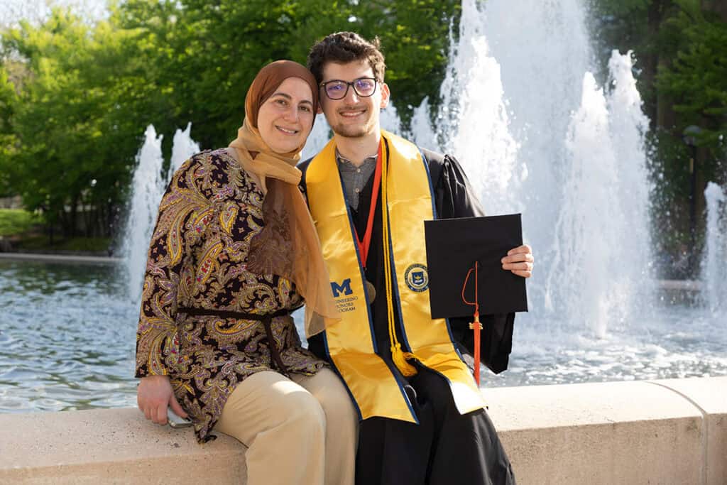 Two people sit at fountain in graduation attire.