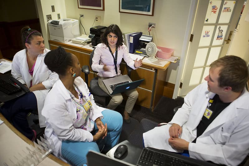 A engineer speaks to a room of three healthcare workers about their process. They are all sitting in chairs in a small room.