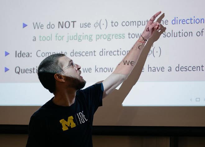 Professor points at slide wearing an IOE shirt