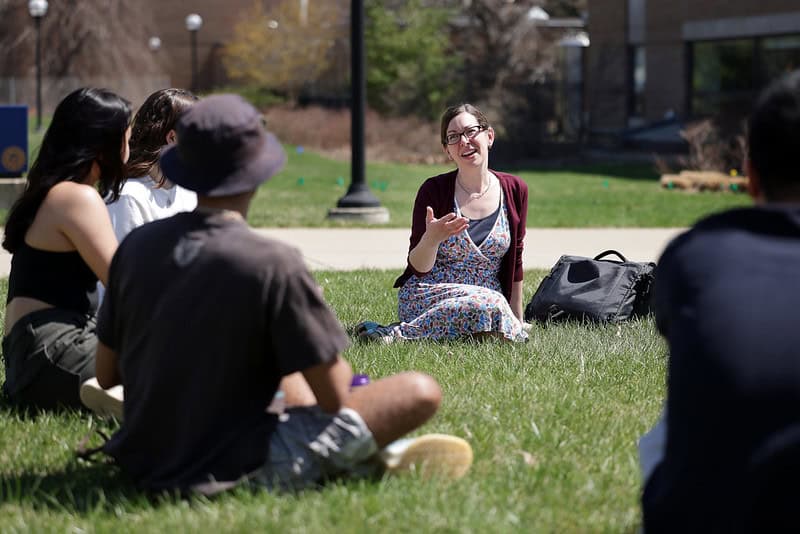 Leia Stirling sits on the grass outside in a circle of other people.