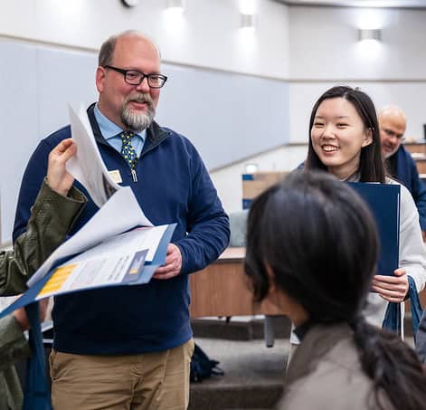 Man wearing professional clothing smiles and speaks to others in the industrial and operations engineering master's.