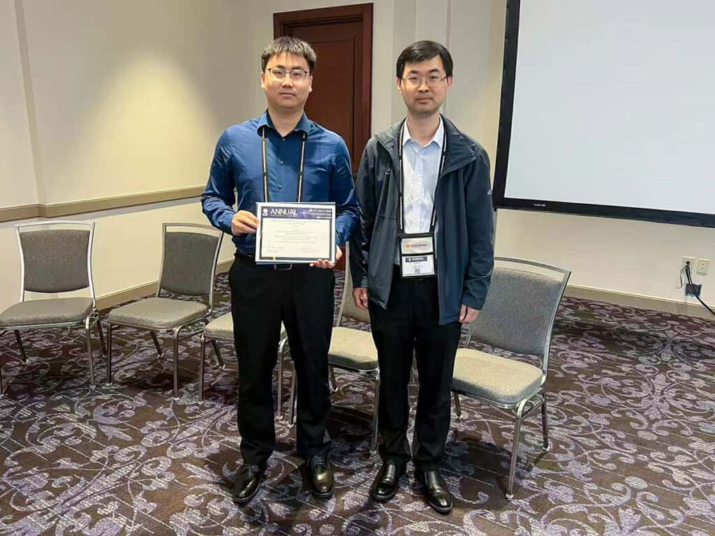 Two people stand next to each other, one holding up an award.