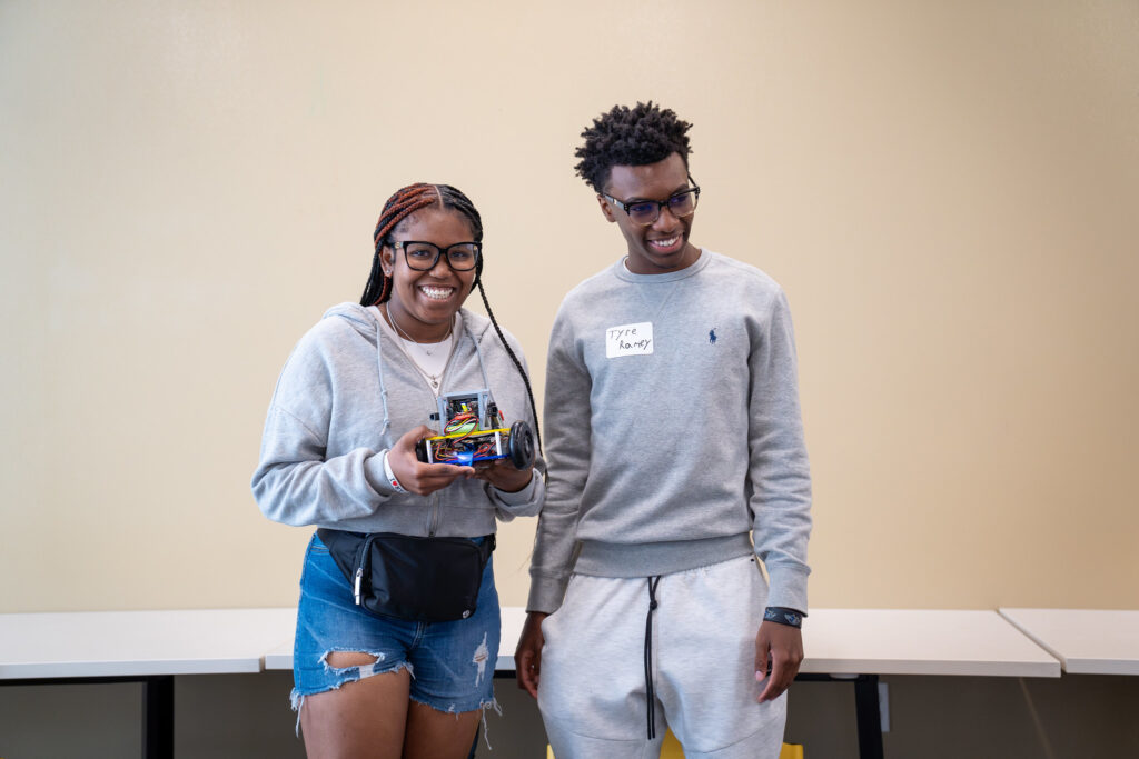 Two students smile and hold a small robot.