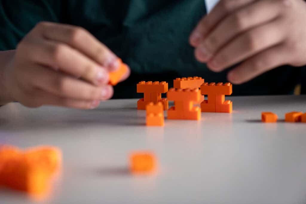 Student assembles orange LEGO bricks on a table.