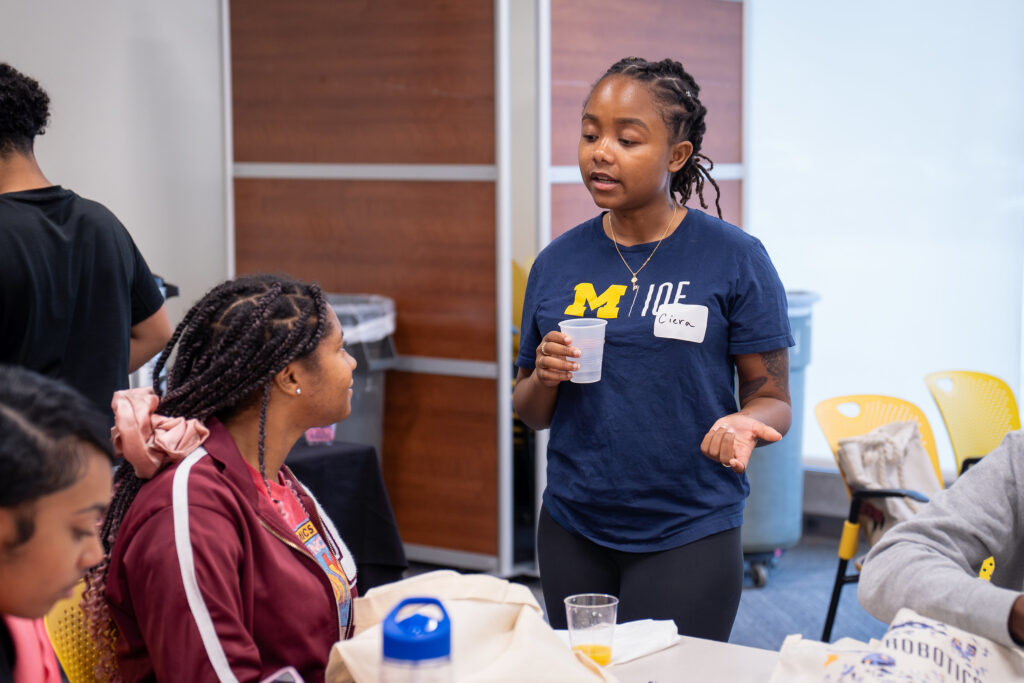 Person wearing a U-M IOE shirt speaks to another person while others converse.